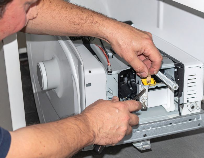 Man fixing a white appliance, using tools to adjust internal components.