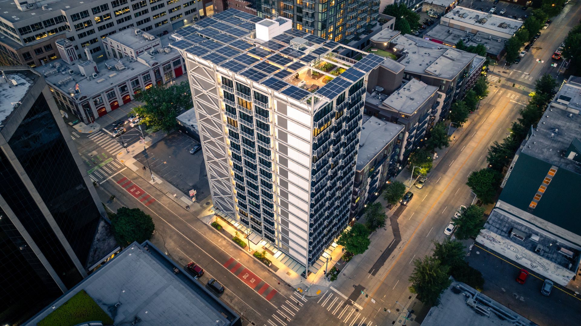 An aerial view of a building with solar panels on the roof in a city.