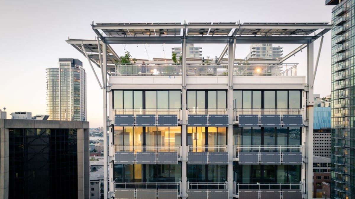 A large building with a lot of windows is surrounded by other buildings.