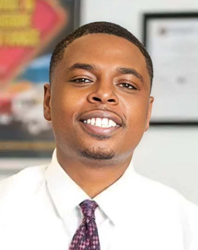 Smiling man in a white shirt and patterned tie, indoors.