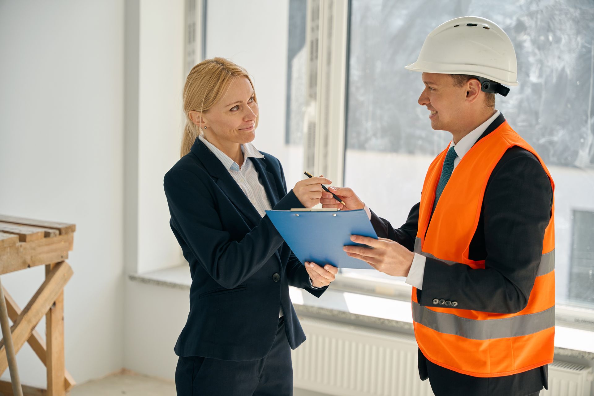Woman in suit signing document for construction worker in hard hat and vest.