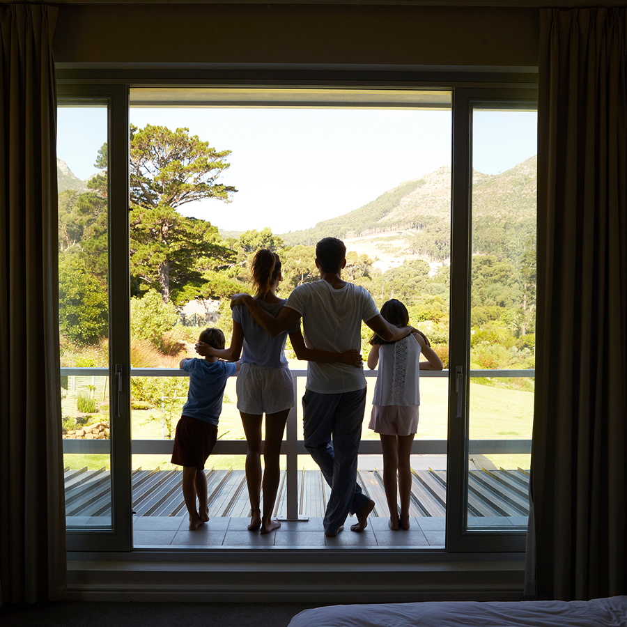Family standing at a sliding glass door, looking at a mountain view.