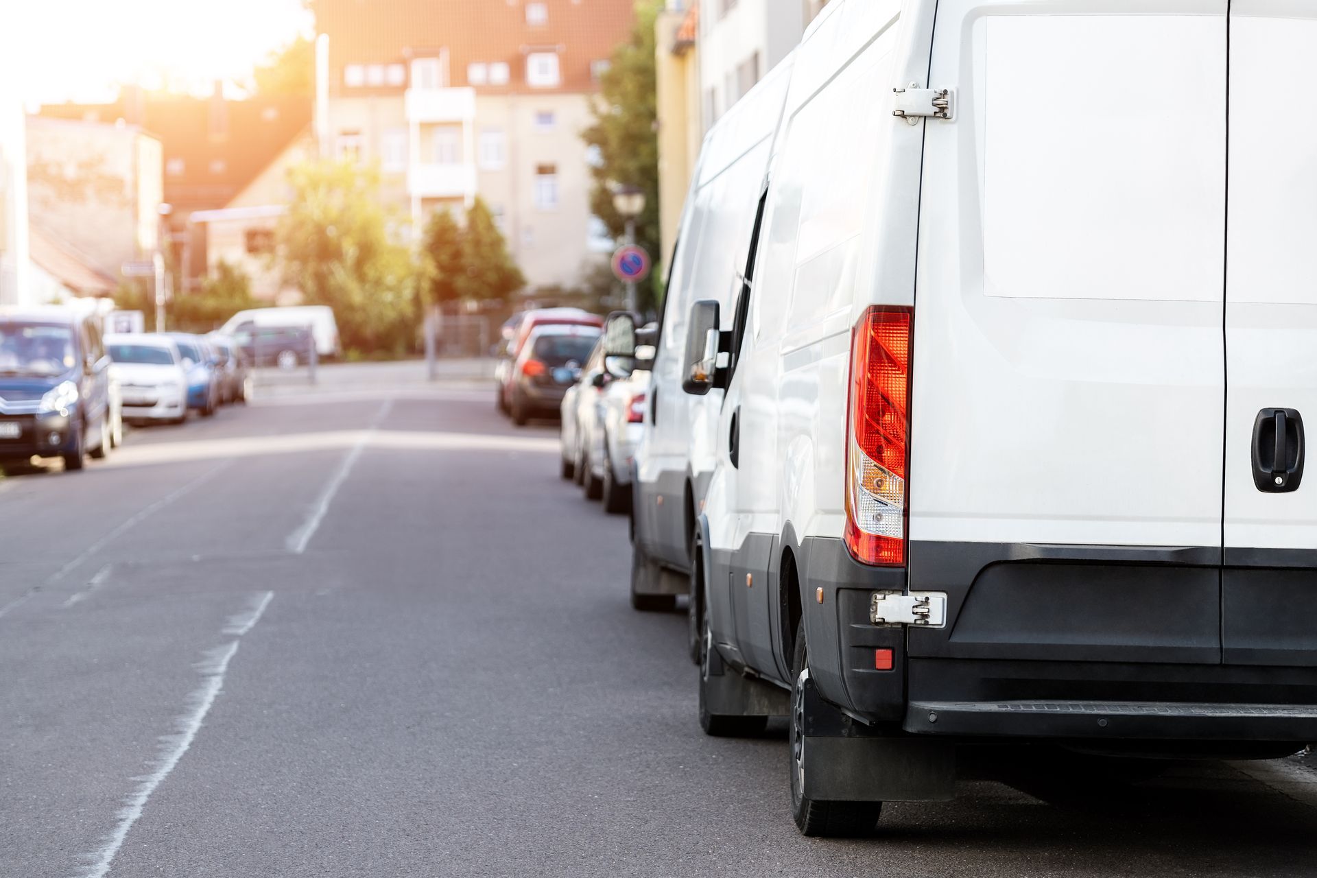 White delivery vans parked along a city street, other cars in the background, sunlit.