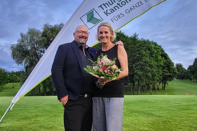 Ein Paar posiert mit einem Blumenstrauss auf einem Golfplatz.