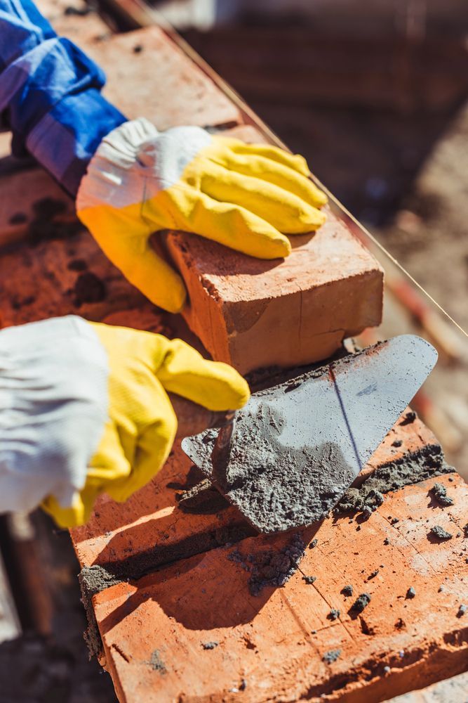 Mani guantate che posizionano un mattone con la malta su una superficie di mattoni durante un lavoro di muratura.