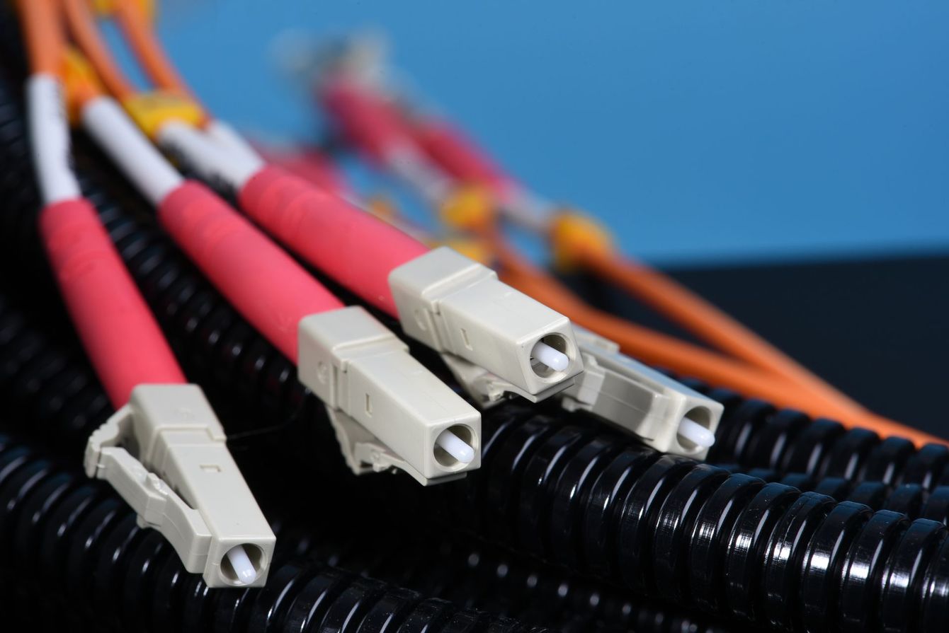 Primo piano di connettori per cavi in ​​fibra ottica con codice colore su una guaina nera corrugata.