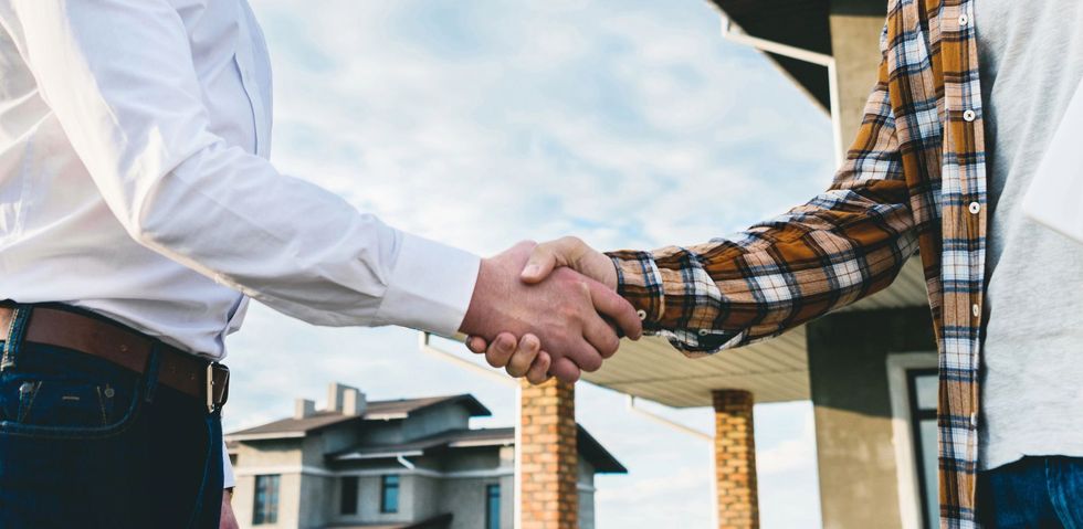 Due persone si stringono la mano all'aperto davanti a una casa in costruzione.
