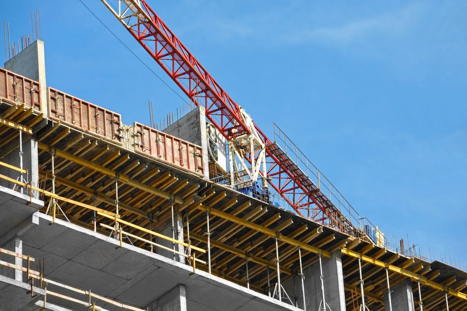 Cantiere edile con casseforme in cemento e gru rossa sullo sfondo di un cielo azzurro.