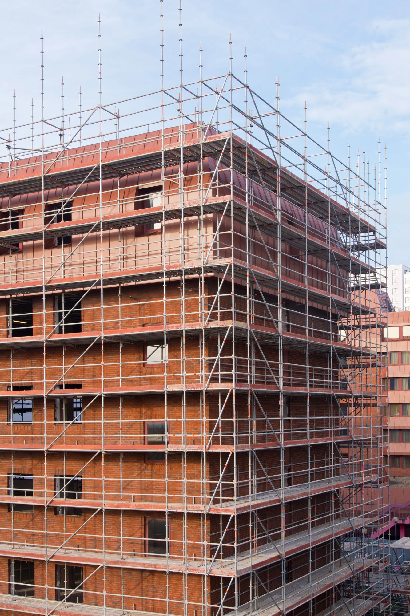 Edificio in mattoni in costruzione, ricoperto da impalcature, sullo sfondo di un cielo azzurro.
