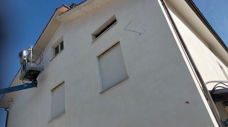Edificio in stucco bianco visto dal basso contro un cielo azzurro, con finestre con persiane e un piccolo ascensore con balcone.