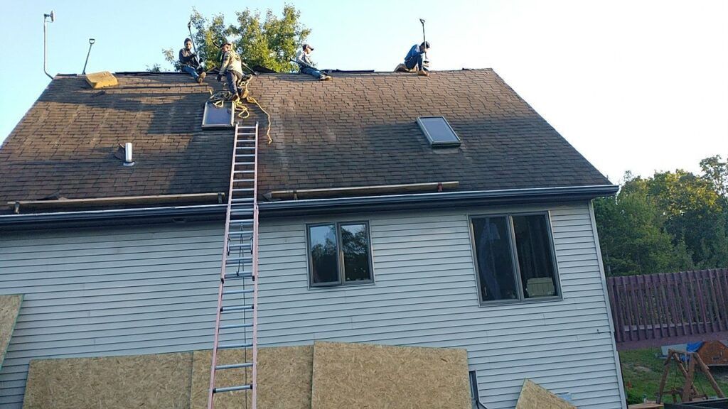 A man on a ladder is working on the roof of a house