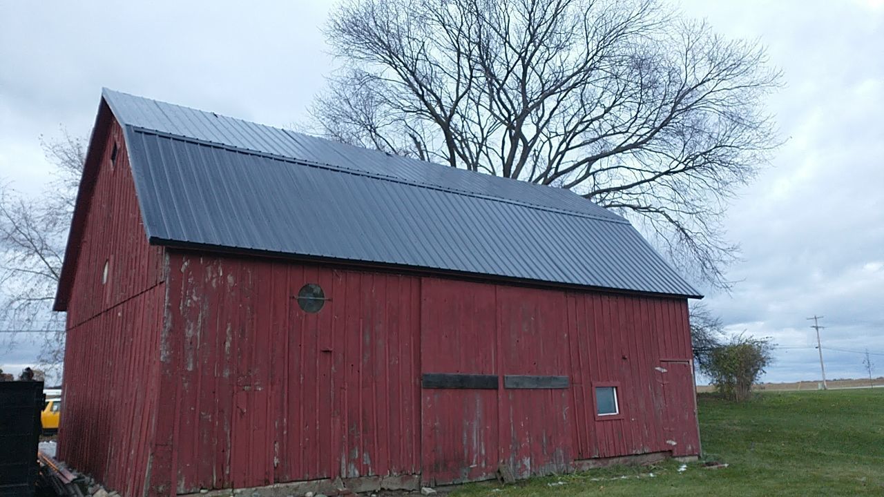 A red barn with a black roof and a tree in the background.