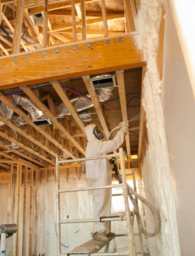 A man is spraying insulation on the ceiling of a house under construction.