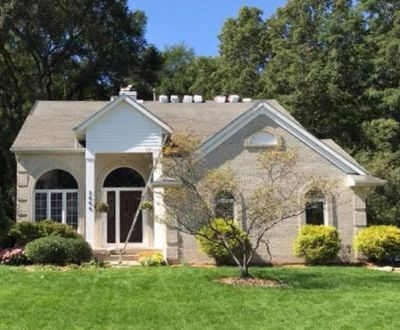 A large white house with a gray roof is sitting on top of a lush green lawn.