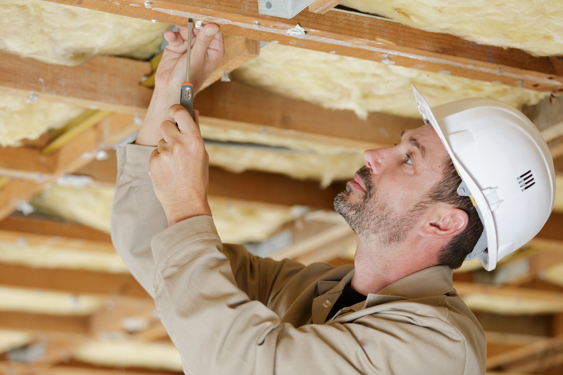 A man wearing a hard hat is working on the ceiling of a house.