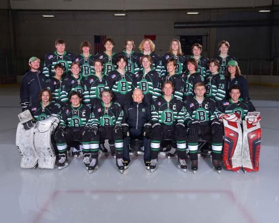 Youth hockey team and coaches posing on an ice rink in black and teal uniforms, with goalie gear at both ends