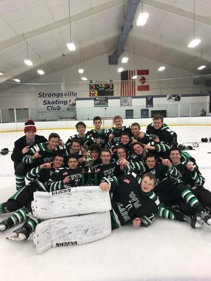 Hockey team in green jerseys posing on the ice in a rink with championship trophies.