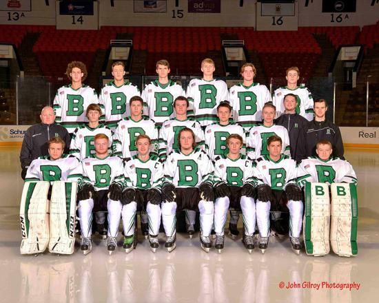 Hockey team group photo in green and white uniforms with goalie pads, posed indoors on the ice
