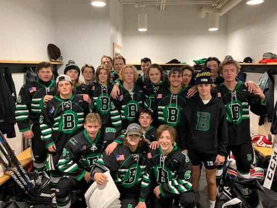 Youth hockey team in black and green uniforms posing together in a locker room