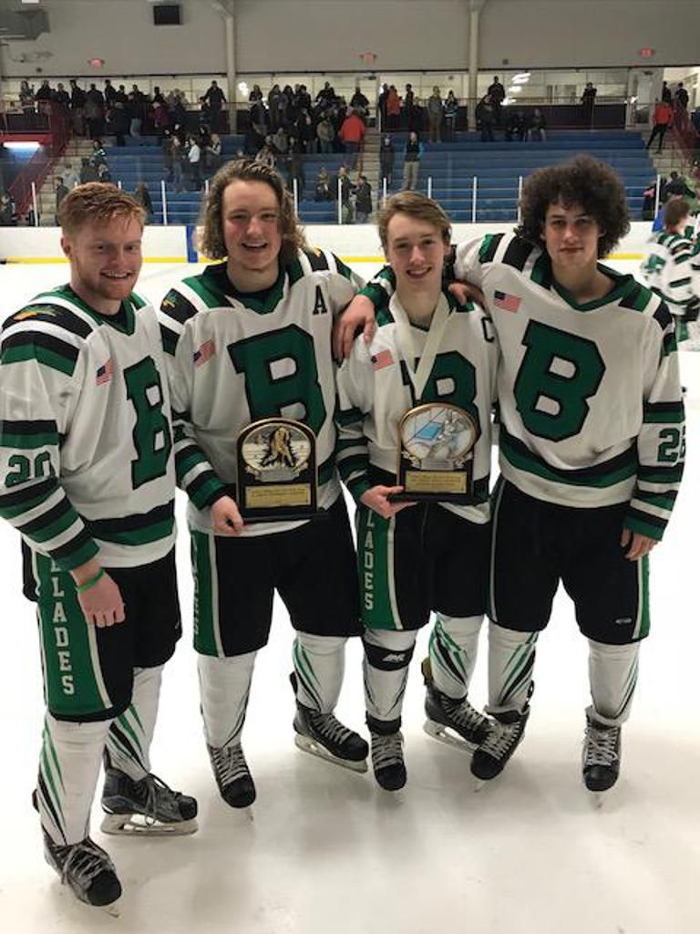 Four hockey players in green-and-white jerseys pose on the ice with trophies.