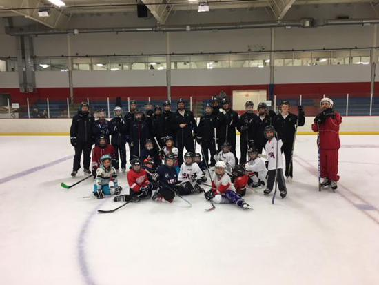 Group of hockey players posing on an indoor ice rink, with a red-suited coach at right.