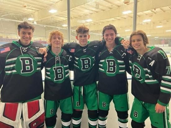 Five hockey players in black and green uniforms posing together on an indoor rink, smiling.