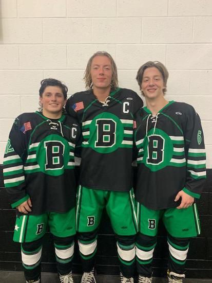 Three hockey players in black and green jerseys posing in front of a white wall.