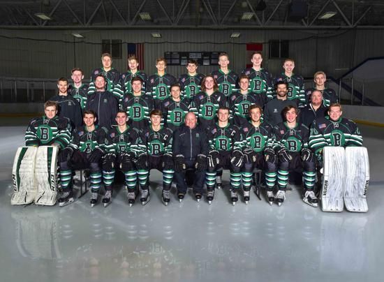 Group of hockey players in green-and-black uniforms posing for a team photo on the ice rink
