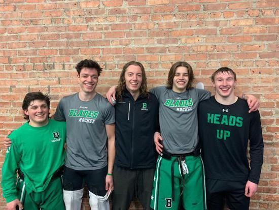 Five smiling teammates in green and black athletic gear posing in front of a brick wall