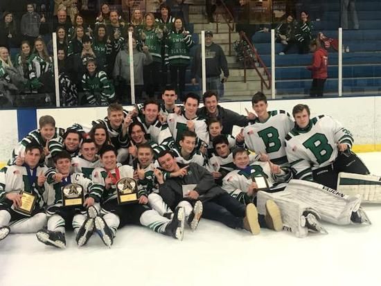 Hockey team poses on the ice after a game, with players in green and white uniforms sitting and kneeling together.