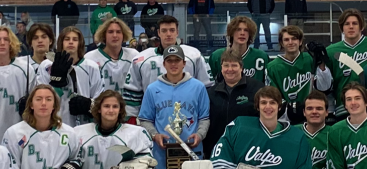 Group of hockey players and coaches in green-and-white jerseys posing for a team photo indoors