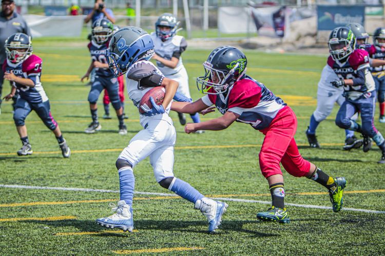 Youth football players in red and white uniforms tackle on a grassy field during a game