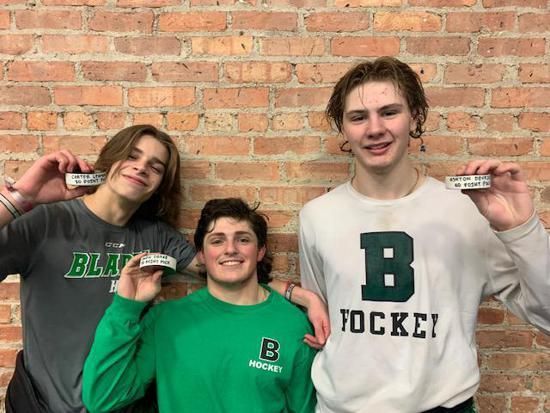 Three athletes in team gear holding medals in front of a brick wall