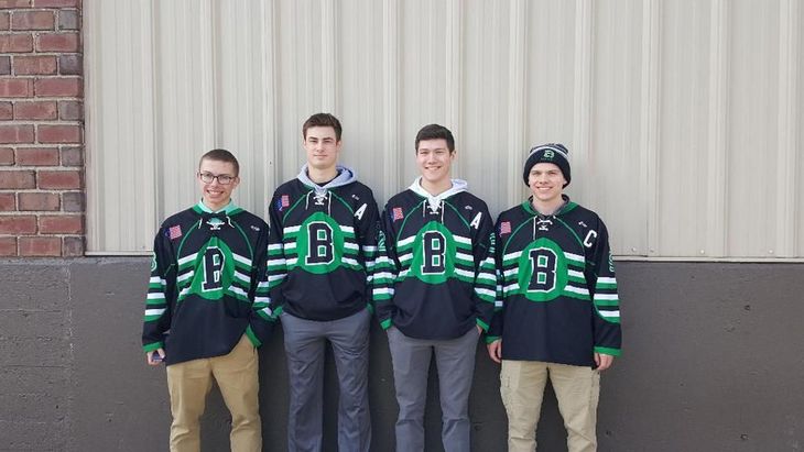 Four hockey players in black and green jerseys standing against a wall