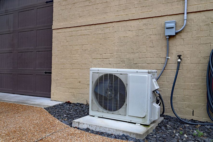Outdoor air-conditioning unit beside a beige house wall and utility pipes
