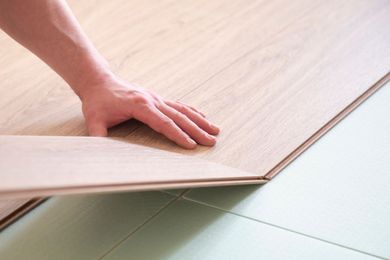 Hand placing a wood-look laminate plank over pale green floor tiles during installation