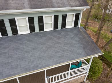 Aerial view of a gray-roofed house with white siding, black shutters, and a covered front porch.