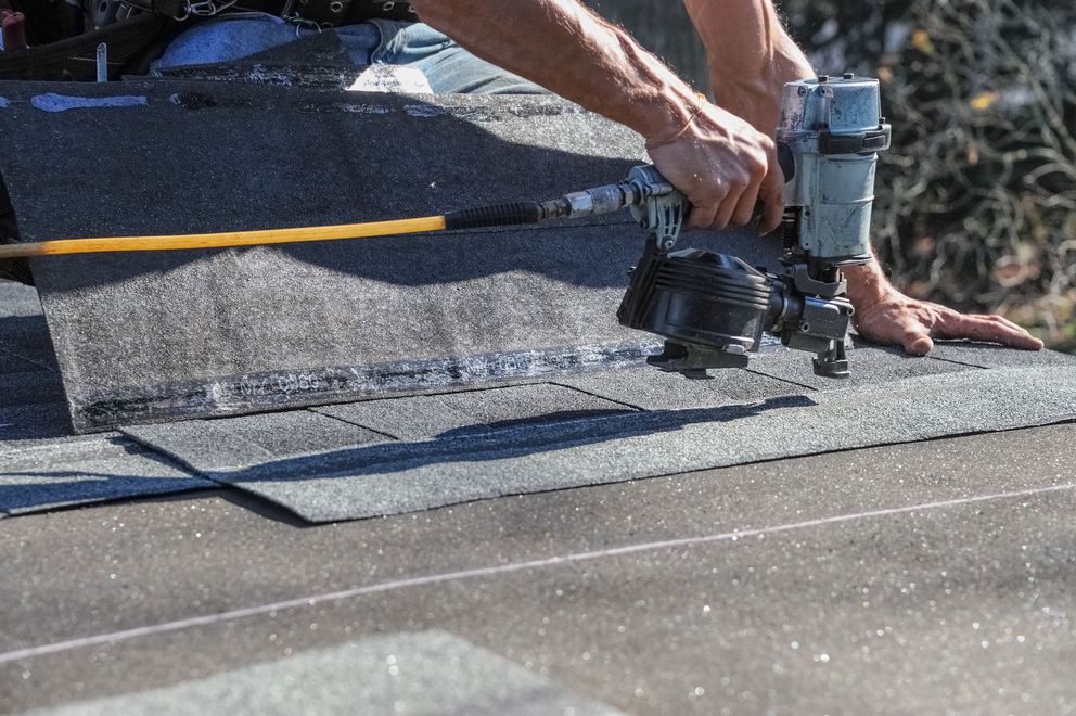 Worker using a nail gun to install roofing shingles on a roof.