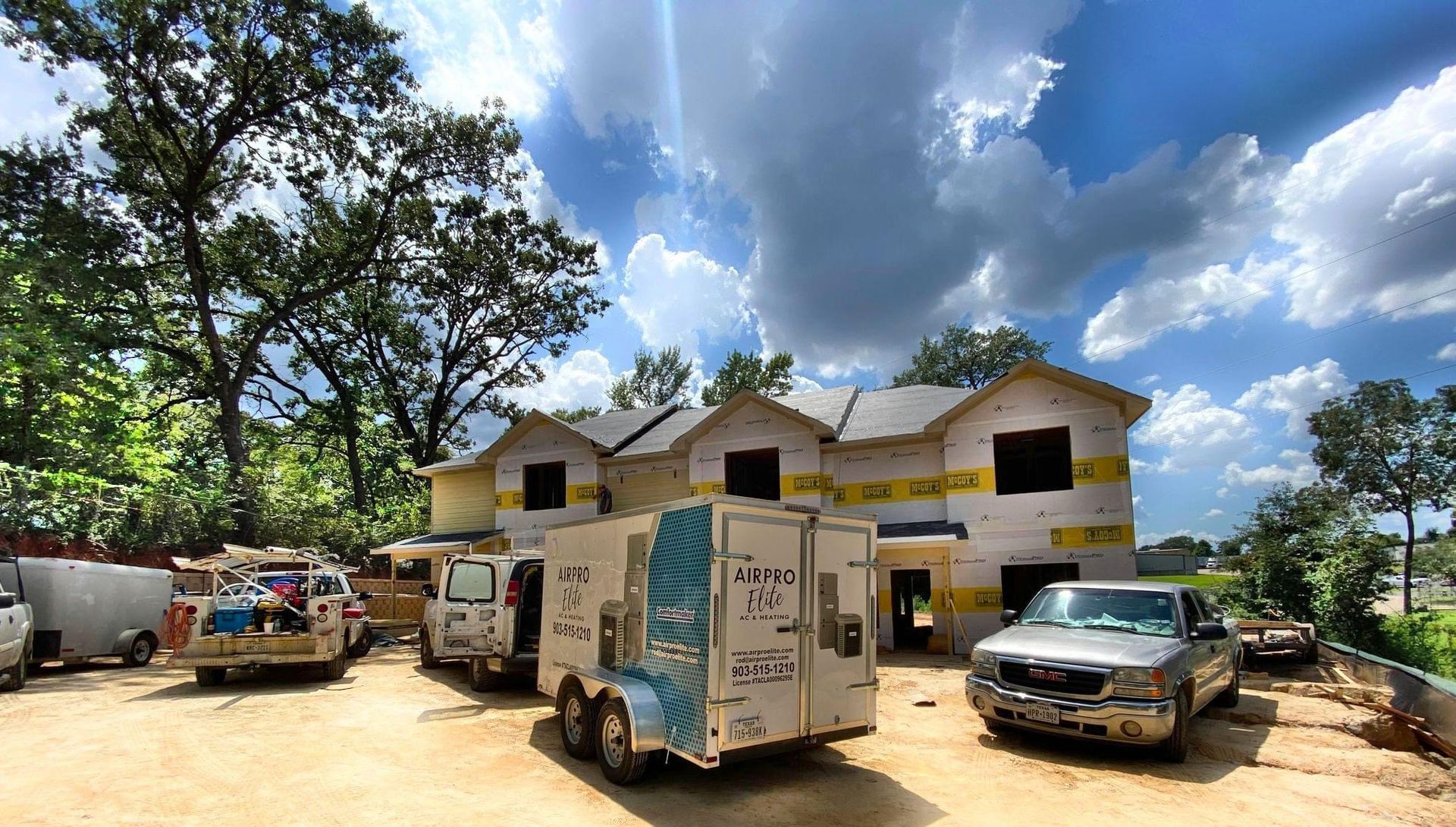 Rural compound with white buildings, parked trucks, and a car under a bright cloudy sky
