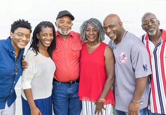 Six smiling people standing together outdoors against a light blue background