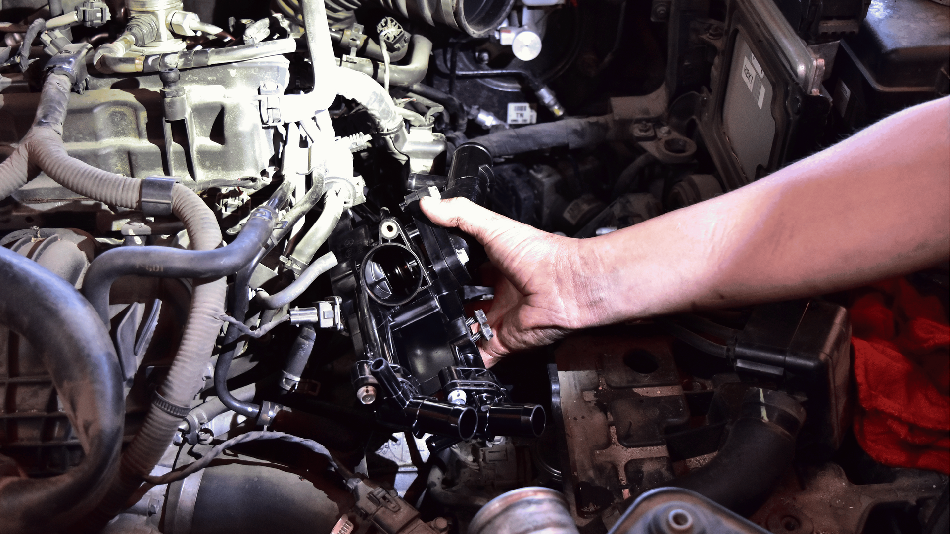 Technician holding thermostat assembly during a cooling system inspection for an overheating engine