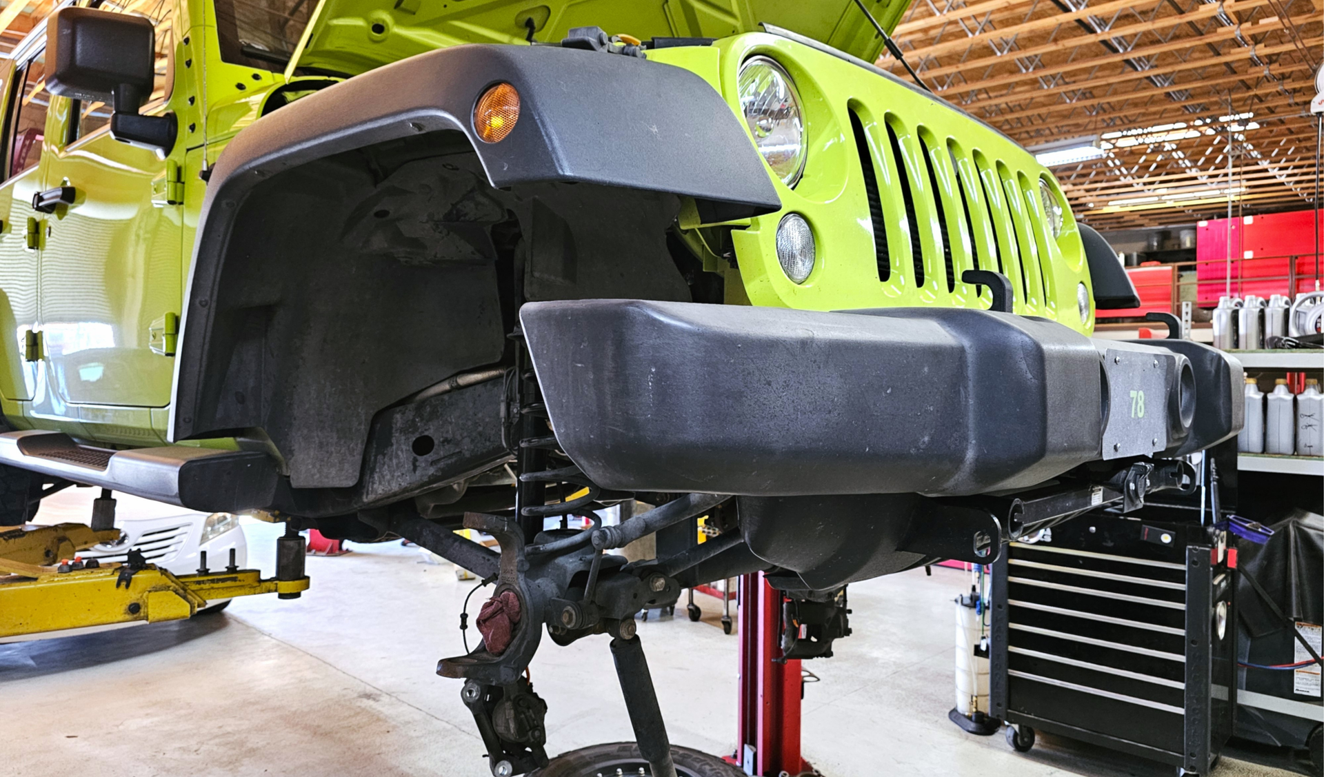 Jeep on lift with front end exposed showing suspension, steering, & wheel components for maintenance