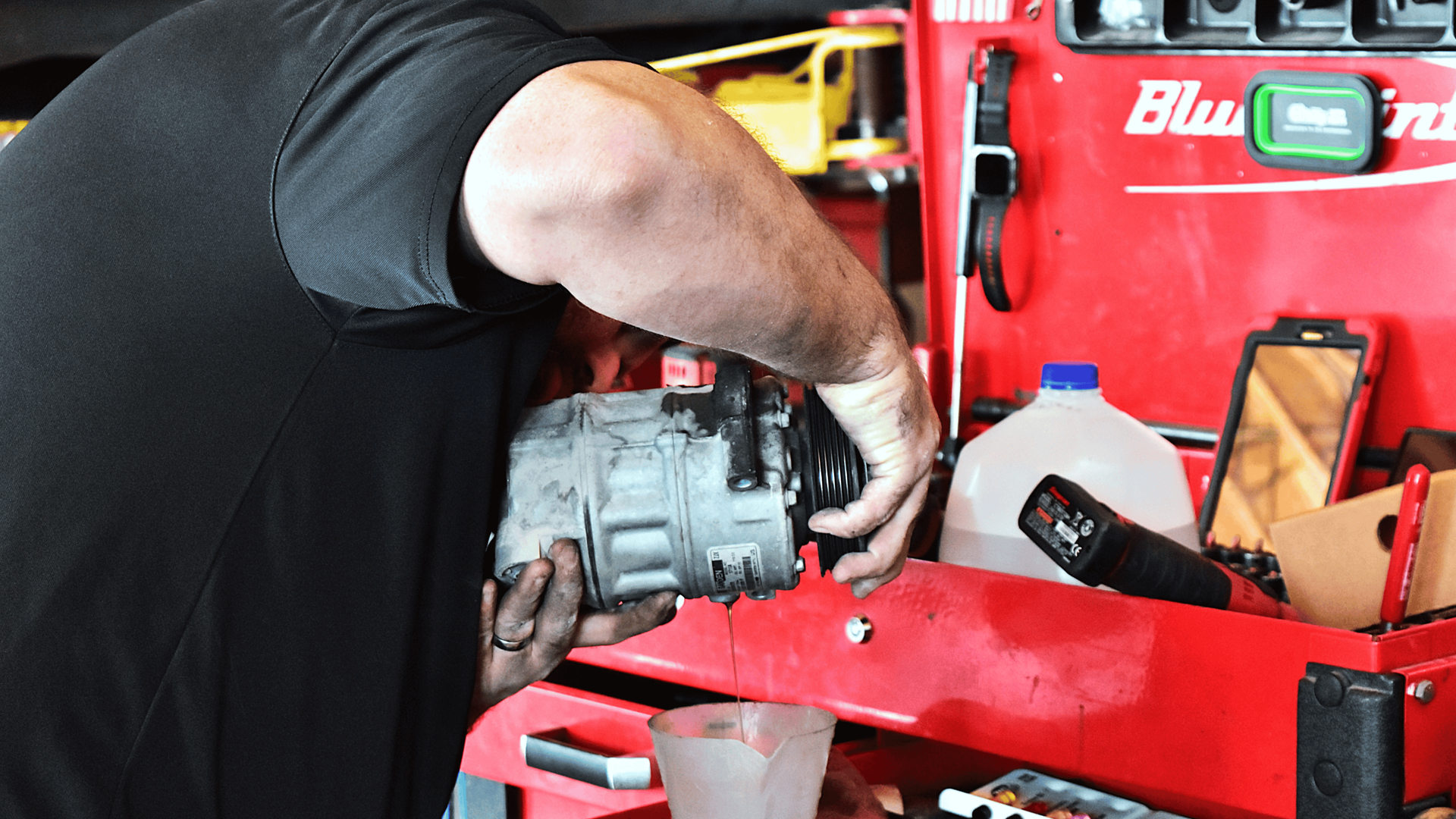 Technician draining A/C compressor oil during automotive A/C repair service in North Phoenix. 