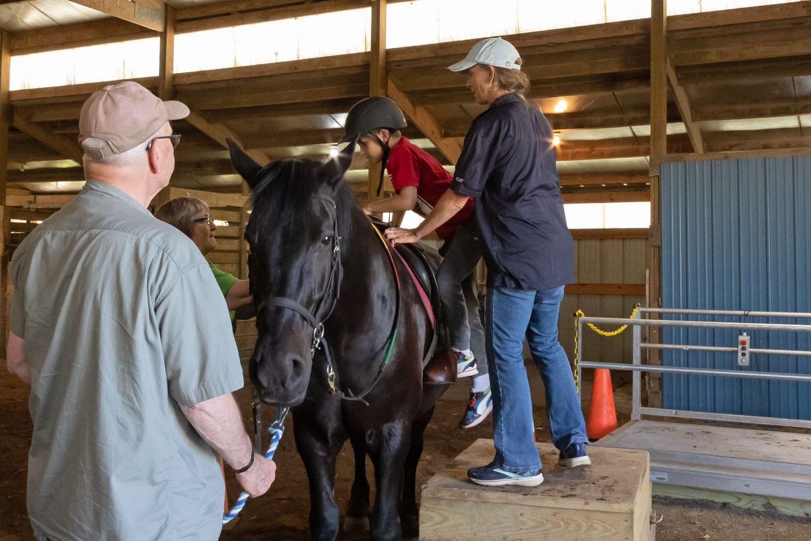 Person on a black horse in an indoor riding arena with two helpers nearby