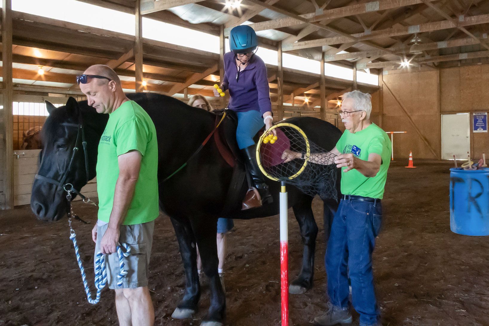 Child riding horse in indoor arena while two adults assist nearby