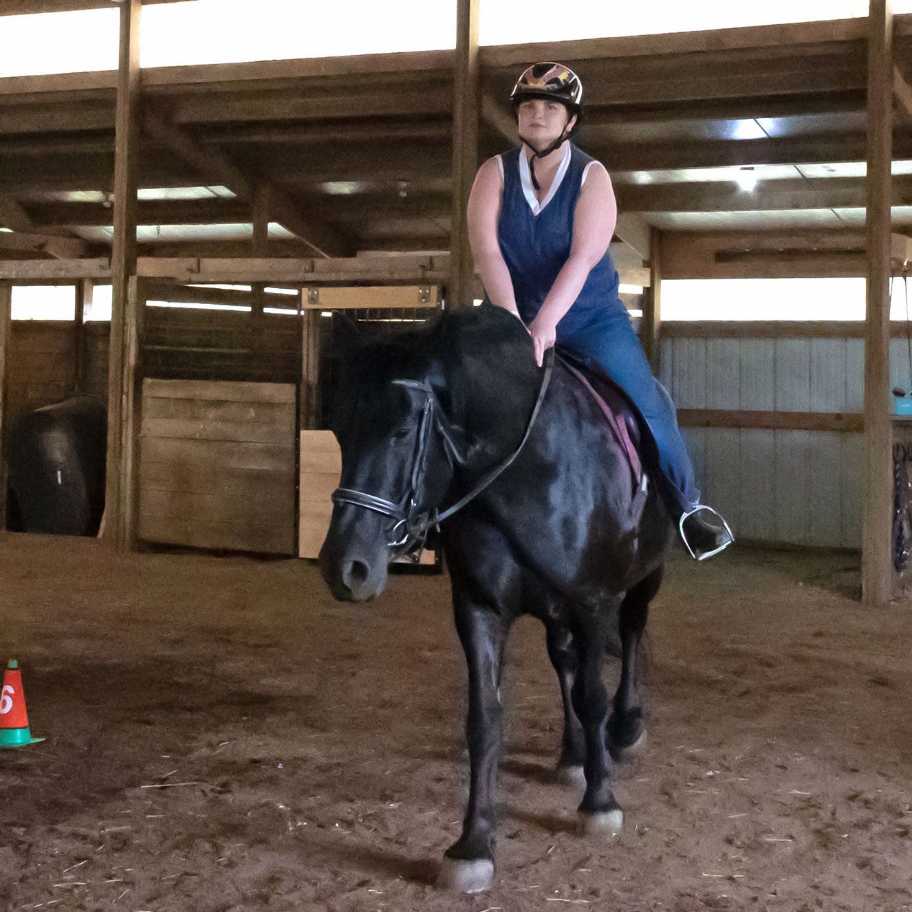 Rider on a black horse in an indoor arena, wearing a helmet and blue shirt.