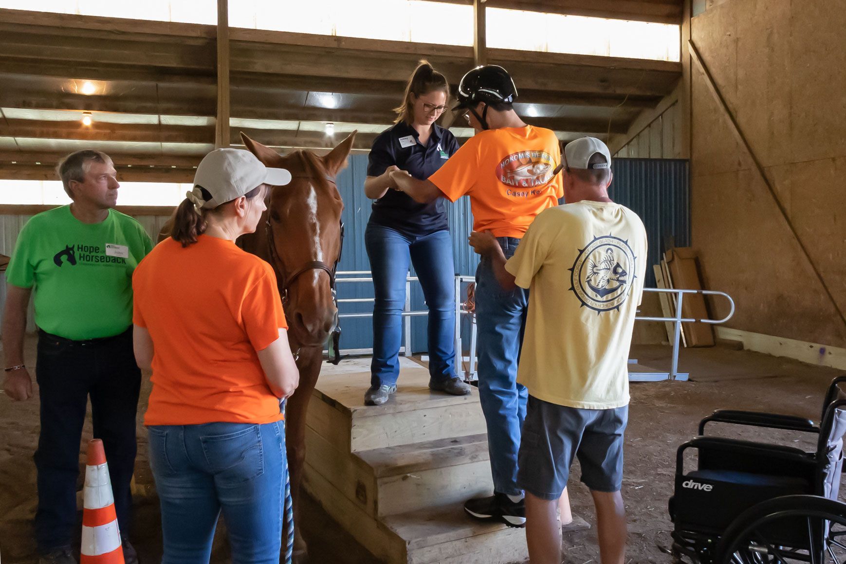 People gathered in a wooden barn, one person handing out orange shirts on a raised platform.