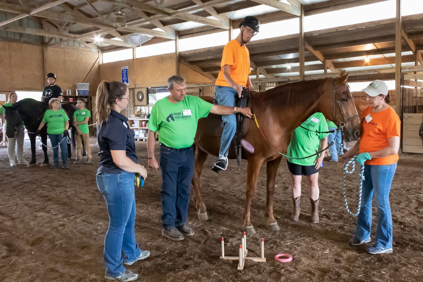 People guiding a child on a horse in a barn, with others standing nearby.