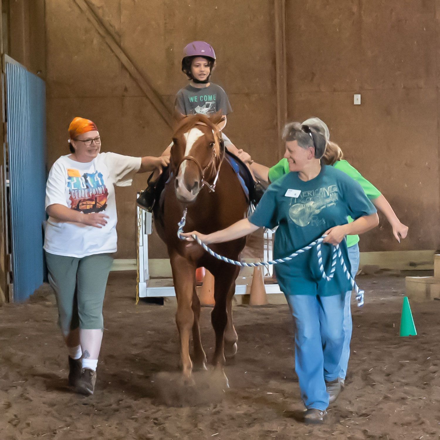 Child on a horse being led by two instructors in an indoor riding arena