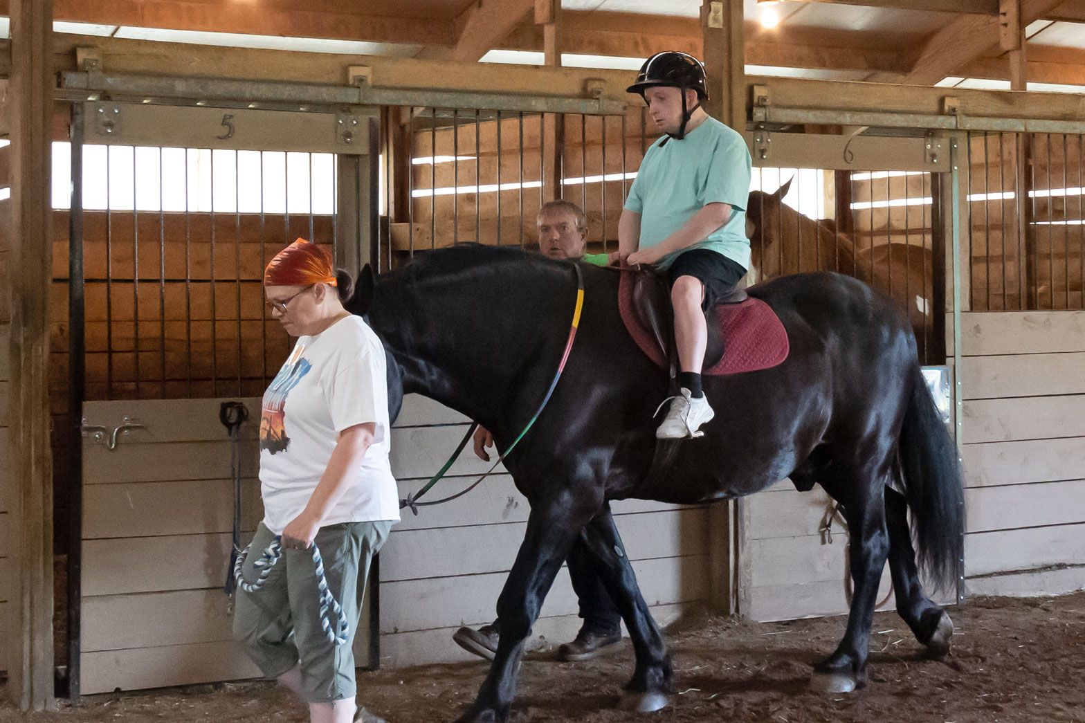 Child riding a black horse indoors while a handler leads it in an arena